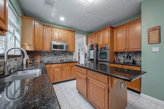 kitchen with dark stone countertops, appliances with stainless steel finishes, sink, a kitchen island, and a kitchen breakfast bar