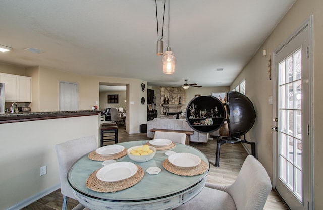 dining room with light hardwood / wood-style floors, ceiling fan, and a stone fireplace