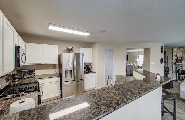 kitchen featuring wood-type flooring, stainless steel appliances, dark stone counters, white cabinets, and a breakfast bar