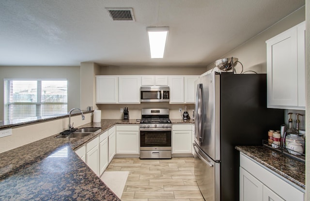 kitchen with white cabinetry, stainless steel appliances, light hardwood / wood-style floors, sink, and dark stone countertops