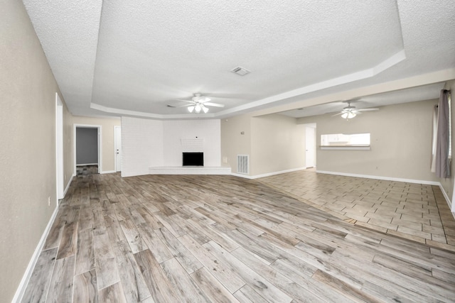 unfurnished living room with a fireplace, ceiling fan, light hardwood / wood-style floors, and a raised ceiling