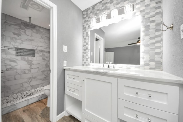 bathroom with hardwood / wood-style flooring, a tile shower, toilet, ceiling fan, and vanity