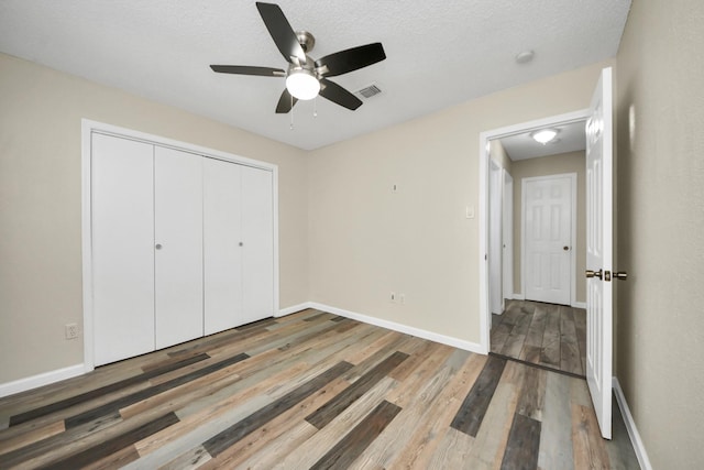 unfurnished bedroom with a textured ceiling, a closet, hardwood / wood-style flooring, and ceiling fan