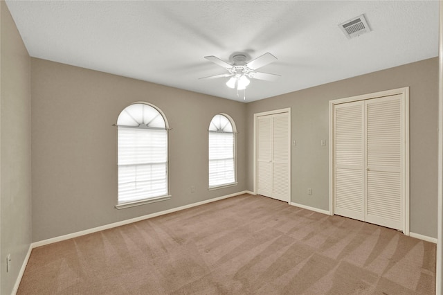 unfurnished bedroom with light carpet, ceiling fan, multiple closets, and a textured ceiling