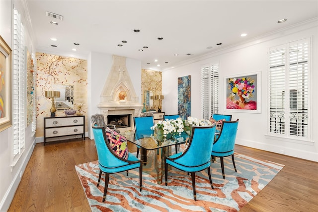 dining space with hardwood / wood-style flooring, ornamental molding, and a fireplace