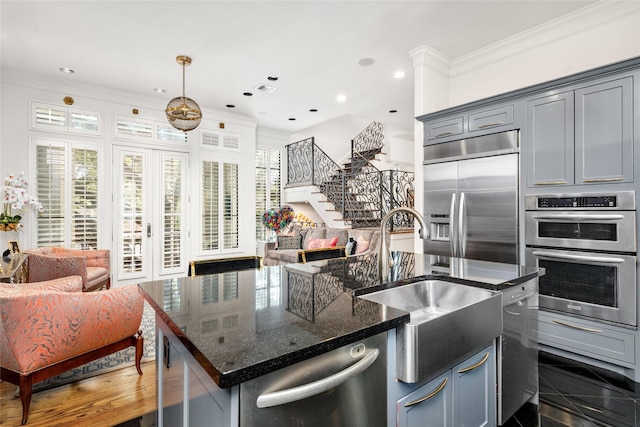 kitchen with a center island with sink, stainless steel appliances, decorative light fixtures, crown molding, and dark stone countertops