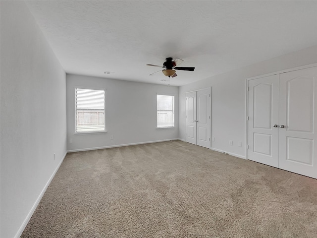 unfurnished bedroom featuring ceiling fan, multiple closets, carpet floors, and a textured ceiling