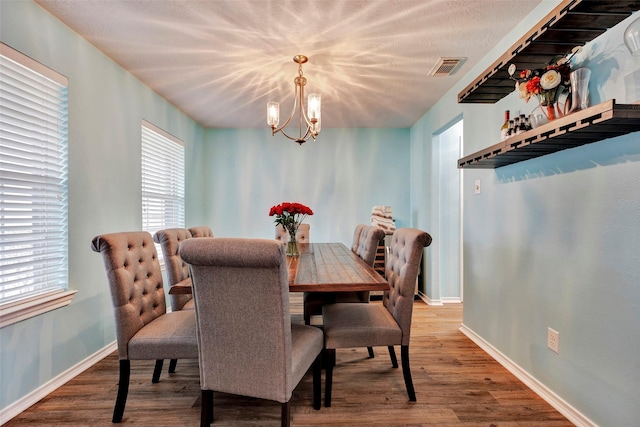 dining room with baseboards, wood finished floors, visible vents, and an inviting chandelier