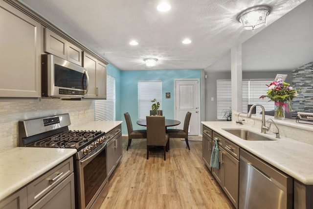 kitchen featuring decorative backsplash, light stone countertops, stainless steel appliances, light wood-type flooring, and a sink