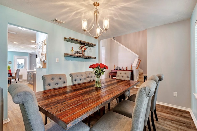 dining room with baseboards, visible vents, wood finished floors, stairs, and a notable chandelier