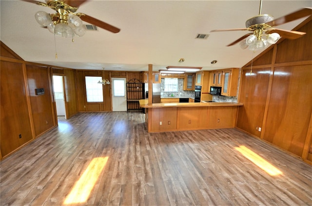 kitchen with vaulted ceiling, wood walls, kitchen peninsula, and hardwood / wood-style floors