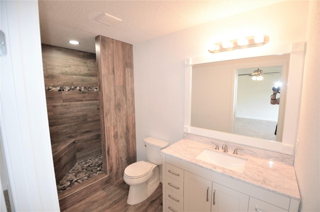 bathroom featuring hardwood / wood-style flooring, toilet, a tile shower, a textured ceiling, and vanity