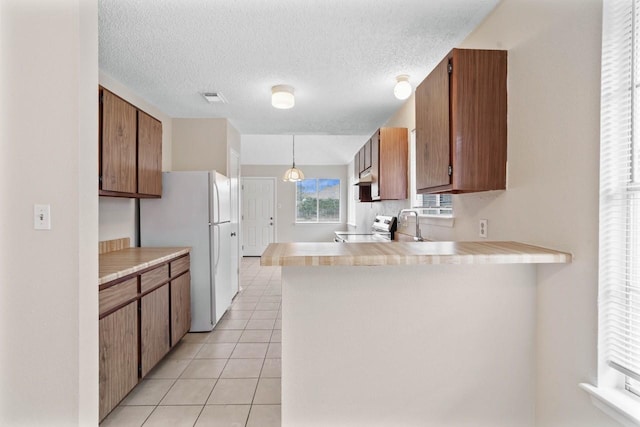 kitchen featuring stainless steel range with electric stovetop, decorative light fixtures, light tile patterned floors, and kitchen peninsula