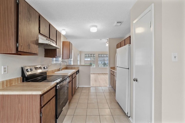 kitchen featuring sink, white fridge, light tile patterned floors, a textured ceiling, and stainless steel range with electric stovetop