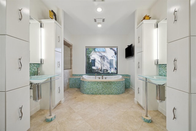 bathroom with two vanities, a sink, visible vents, a bath, and decorative backsplash