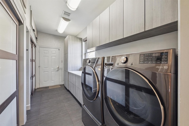 laundry area featuring visible vents, cabinet space, washer and clothes dryer, and dark tile patterned floors