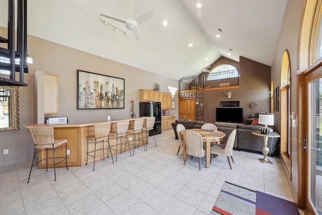 dining area with ceiling fan, high vaulted ceiling, light tile patterned floors, bar area, and baseboards