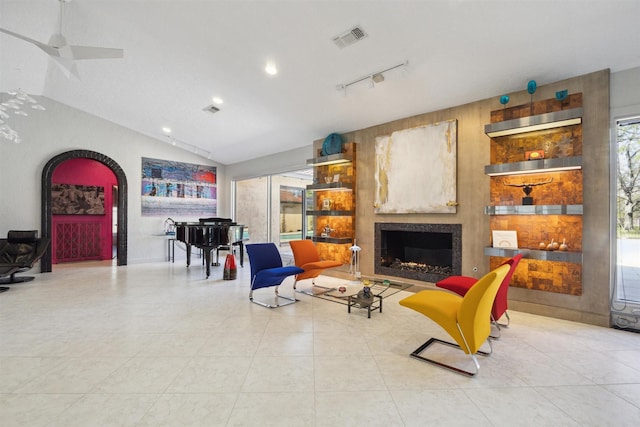 living area with arched walkways, light tile patterned floors, visible vents, vaulted ceiling, and a warm lit fireplace