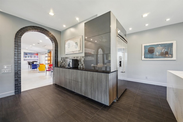 interior space featuring arched walkways, open floor plan, modern cabinets, built in refrigerator, and baseboards