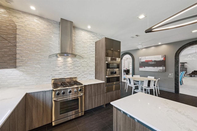 kitchen featuring arched walkways, wall chimney exhaust hood, appliances with stainless steel finishes, and modern cabinets