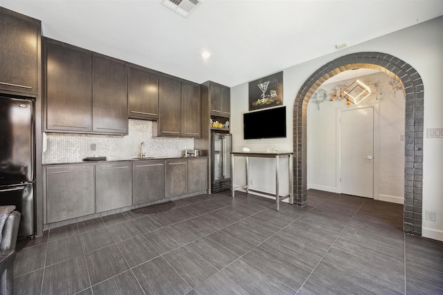 kitchen featuring a sink, visible vents, dark brown cabinets, backsplash, and freestanding refrigerator