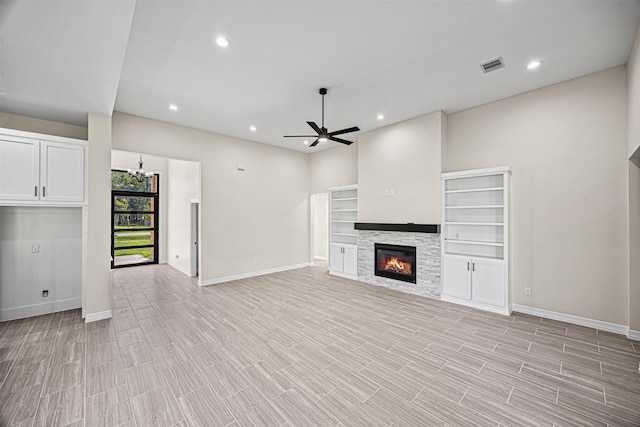 unfurnished living room with ceiling fan with notable chandelier, a stone fireplace, and light hardwood / wood-style floors