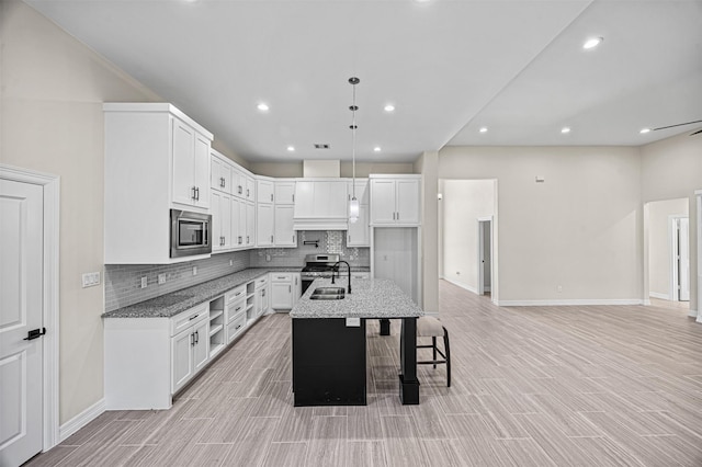 kitchen with light stone countertops, a kitchen island with sink, white cabinets, and stainless steel appliances