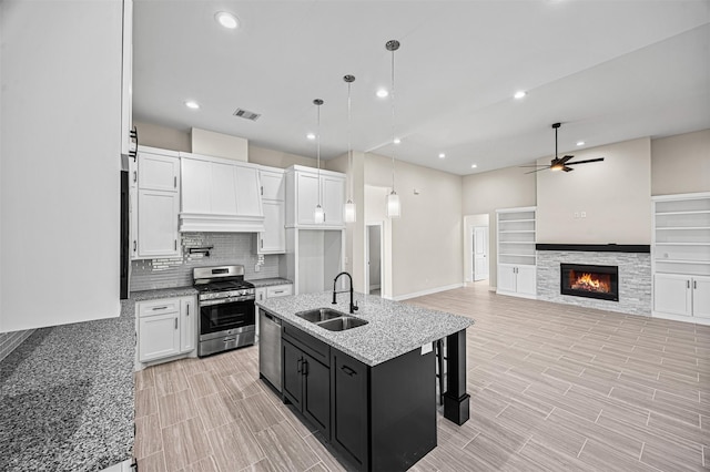 kitchen featuring appliances with stainless steel finishes, sink, white cabinets, hanging light fixtures, and an island with sink