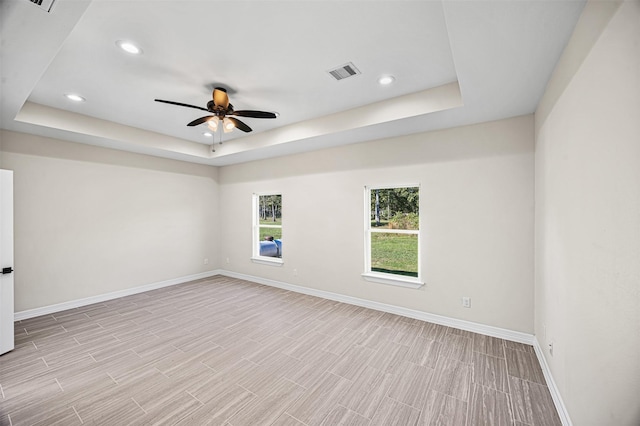 empty room featuring a tray ceiling, ceiling fan, and light hardwood / wood-style flooring