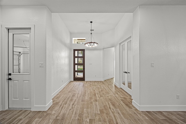 foyer with a chandelier, french doors, baseboards, and light wood finished floors