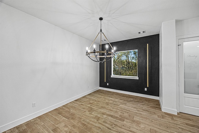 unfurnished dining area featuring an inviting chandelier and wood-type flooring