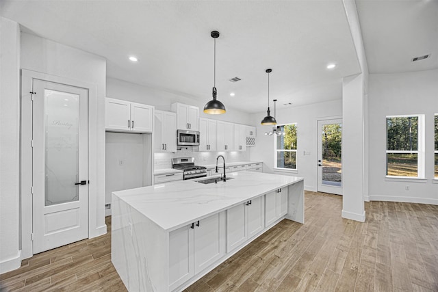 kitchen featuring an island with sink, white cabinetry, stainless steel appliances, and light stone counters