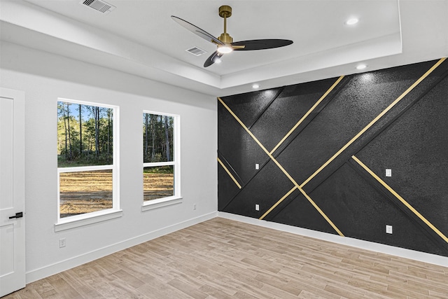 empty room with a raised ceiling, wood finished floors, visible vents, and baseboards