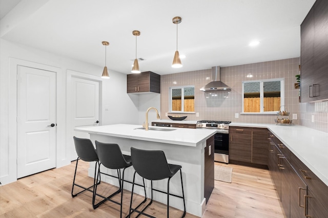 kitchen featuring gas stove, sink, wall chimney range hood, an island with sink, and decorative backsplash