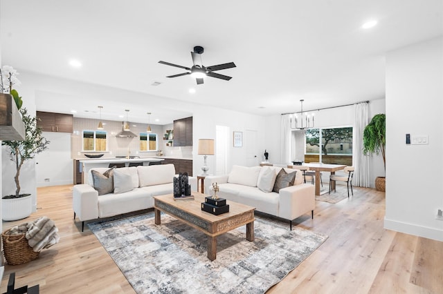 living room with ceiling fan with notable chandelier and light wood-type flooring