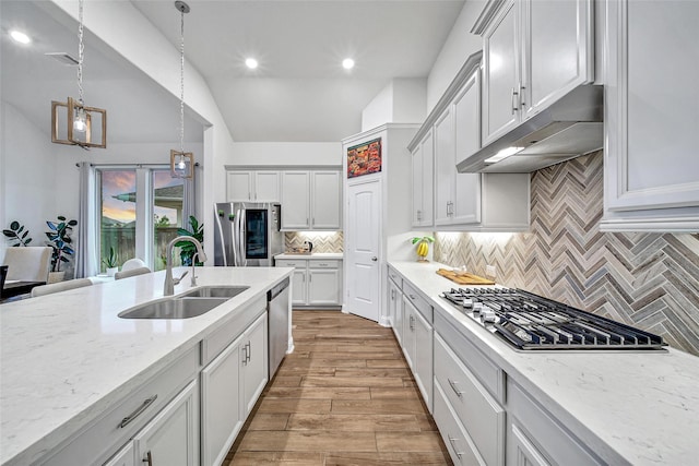 kitchen with light hardwood / wood-style flooring, stainless steel appliances, light stone countertops, decorative light fixtures, and sink