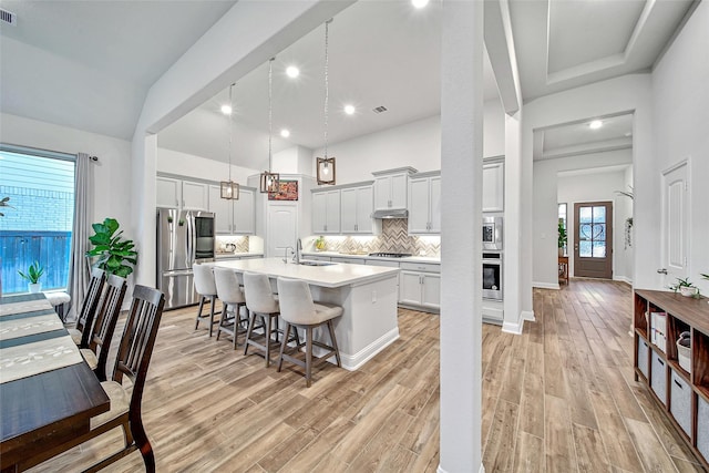 kitchen with appliances with stainless steel finishes, a kitchen breakfast bar, decorative light fixtures, sink, and a kitchen island with sink