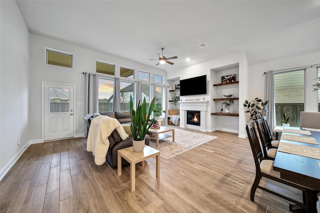 living room featuring built in features, light hardwood / wood-style flooring, ceiling fan, and a wealth of natural light