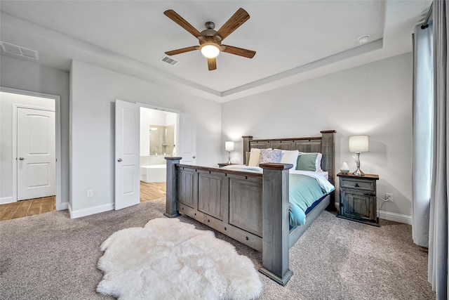 carpeted bedroom with a tray ceiling, ceiling fan, and ensuite bathroom