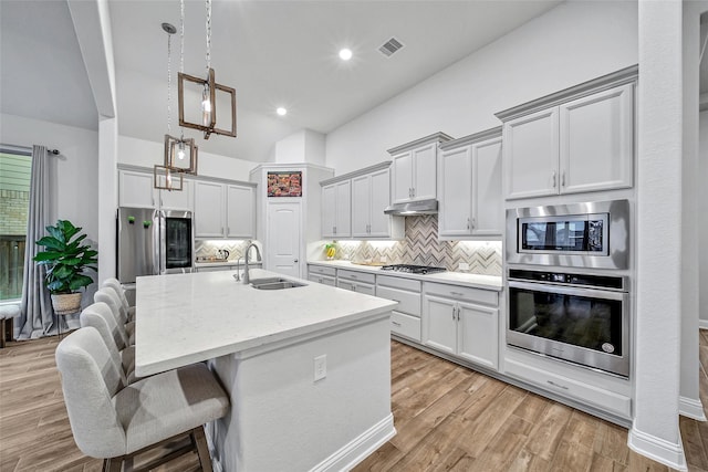 kitchen featuring a center island with sink, stainless steel appliances, light stone counters, pendant lighting, and sink