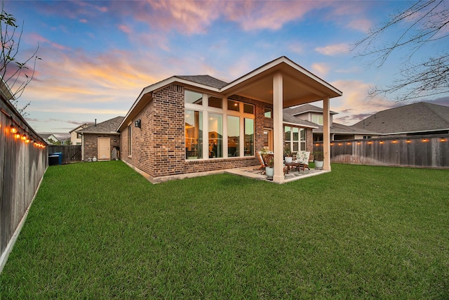 back house at dusk with a patio and a lawn