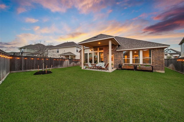 back house at dusk featuring a yard and a patio