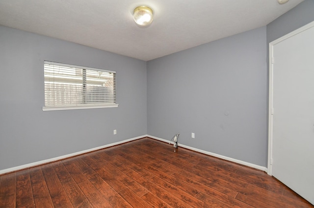 spare room with baseboards and dark wood-style flooring