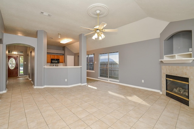 unfurnished living room featuring light tile patterned floors, lofted ceiling, ceiling fan, a tile fireplace, and baseboards