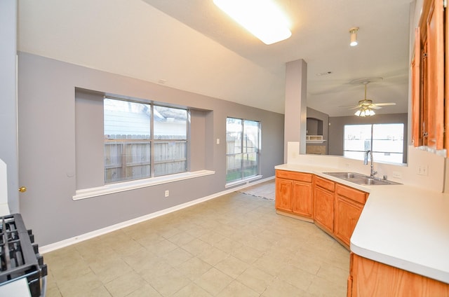 kitchen featuring ceiling fan, a sink, vaulted ceiling, light countertops, and brown cabinetry