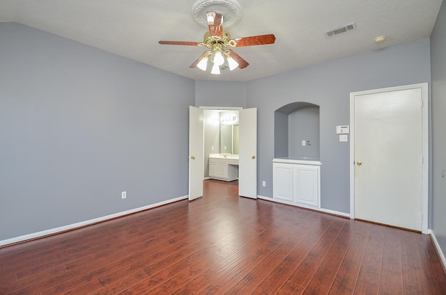 unfurnished bedroom featuring arched walkways, visible vents, dark wood finished floors, and baseboards