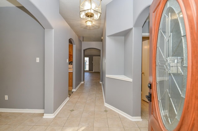 hall with arched walkways, light tile patterned floors, an inviting chandelier, and baseboards