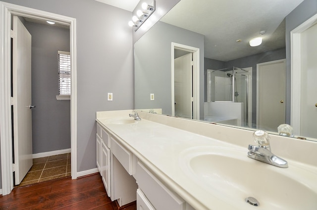 bathroom featuring wood finished floors, a sink, a shower stall, and double vanity