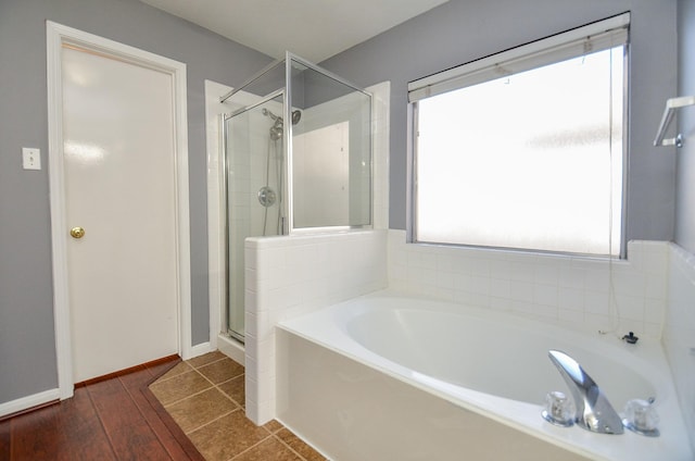 full bathroom with a stall shower, wood finished floors, a bath, and baseboards