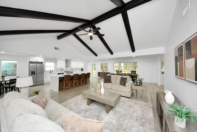 living room featuring high vaulted ceiling, beamed ceiling, a wealth of natural light, and light hardwood / wood-style flooring